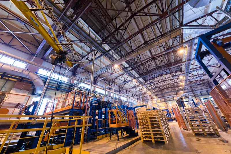 Vue intérieure d'une usine industrielle avec des équipements de production lourde et des palettes empilées.