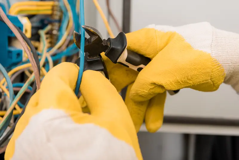 Outils d'électricien jaunes isolés coupant un câble bleu, illustrant les travaux de maintenance électrique et la sécurité dans le bâtiment.