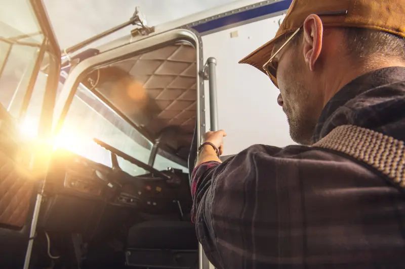 Chauffeur de camion portant une casquette et une veste marron vérifiant les équipements de son gros véhicule de transport.