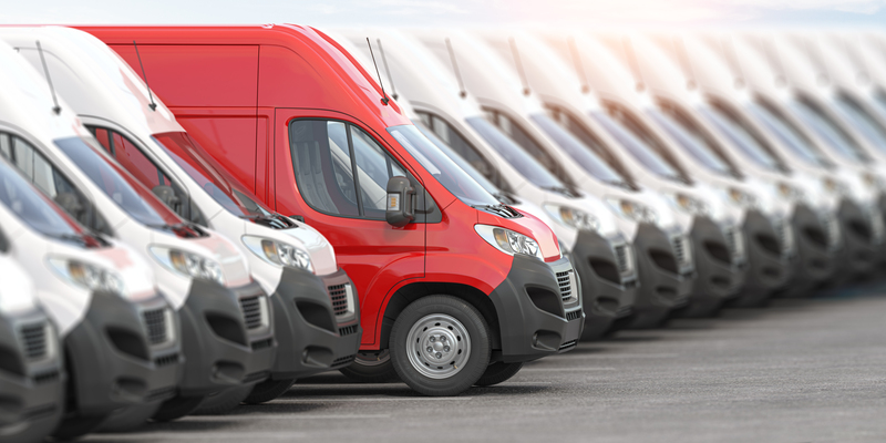 Une rangée de camionnettes de livraison blanches et rouges alignées dans un parking, témoignant de l'uniformité et de l'état de préparation de la flotte.