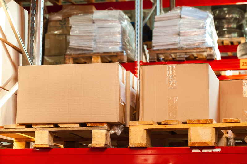 Des piles de grands cartons bien rangés sur des palettes en bois dans un entrepôt.