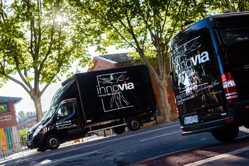 Fourgonnettes de logistique Innovia dans une rue bordée d'arbres démontrant des services de livraison réguliers fiables en milieu urbain.