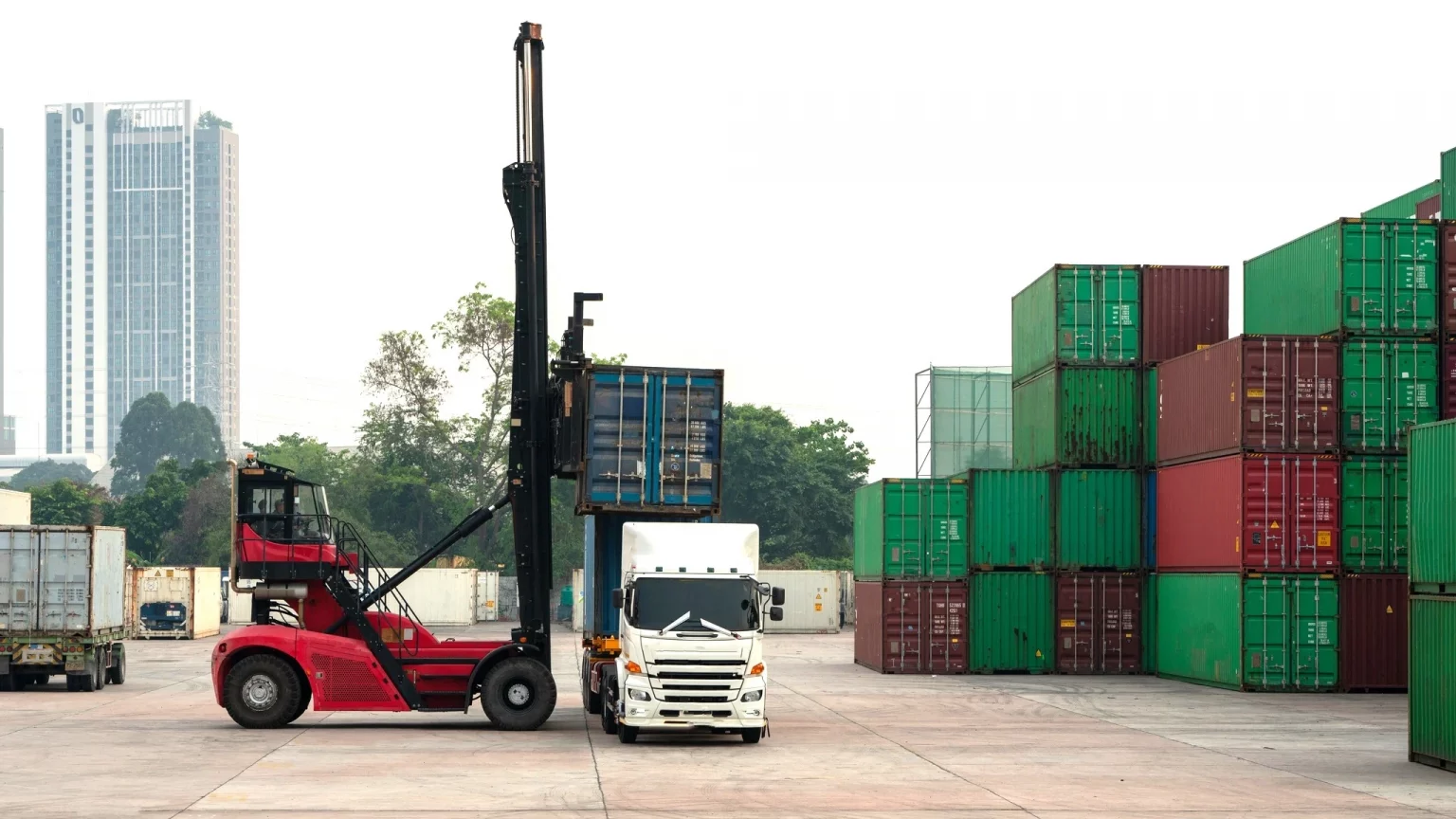 Chariot élévateur rouge chargeant un conteneur bleu dans un terminal de conteneurs, représentant les opérations de manutention et de logistique.