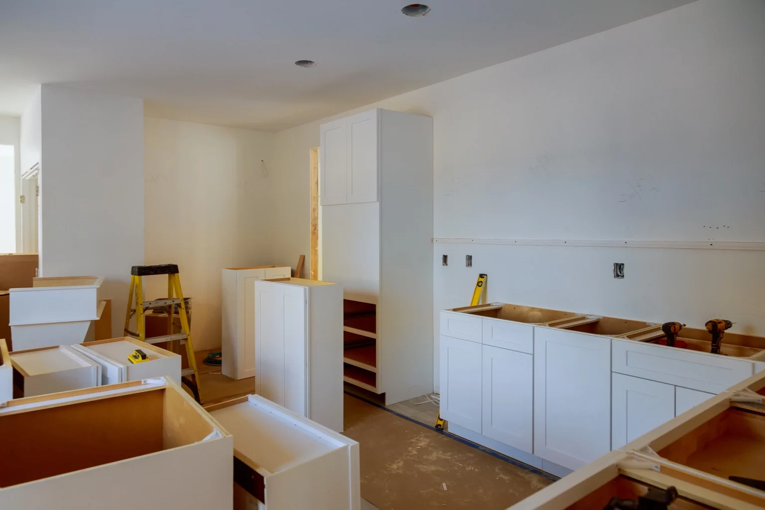 Cuisine en cours de rénovation montrant des armoires blanches partiellement installées et un espace ouvert, illustrant le processus de modernisation d'intérieur.