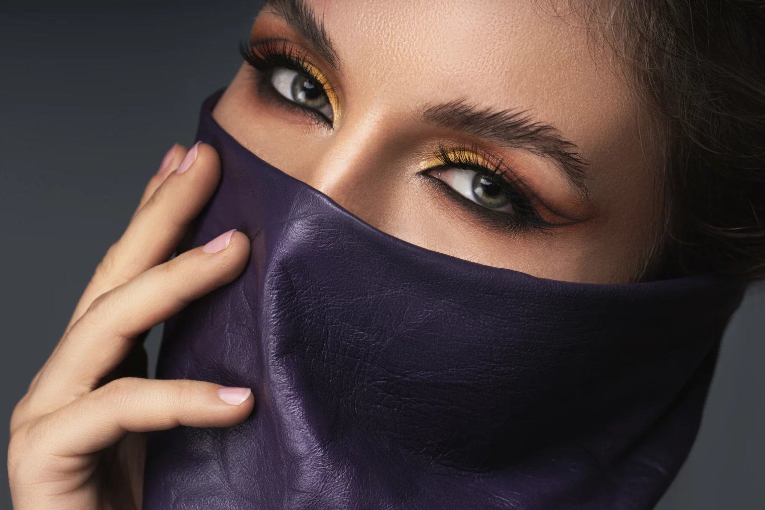 Portrait d'une femme élégante aux yeux maquillés, son visage partiellement voilé par un cache-cou en cuir violet, évoquant le luxe et la mode.