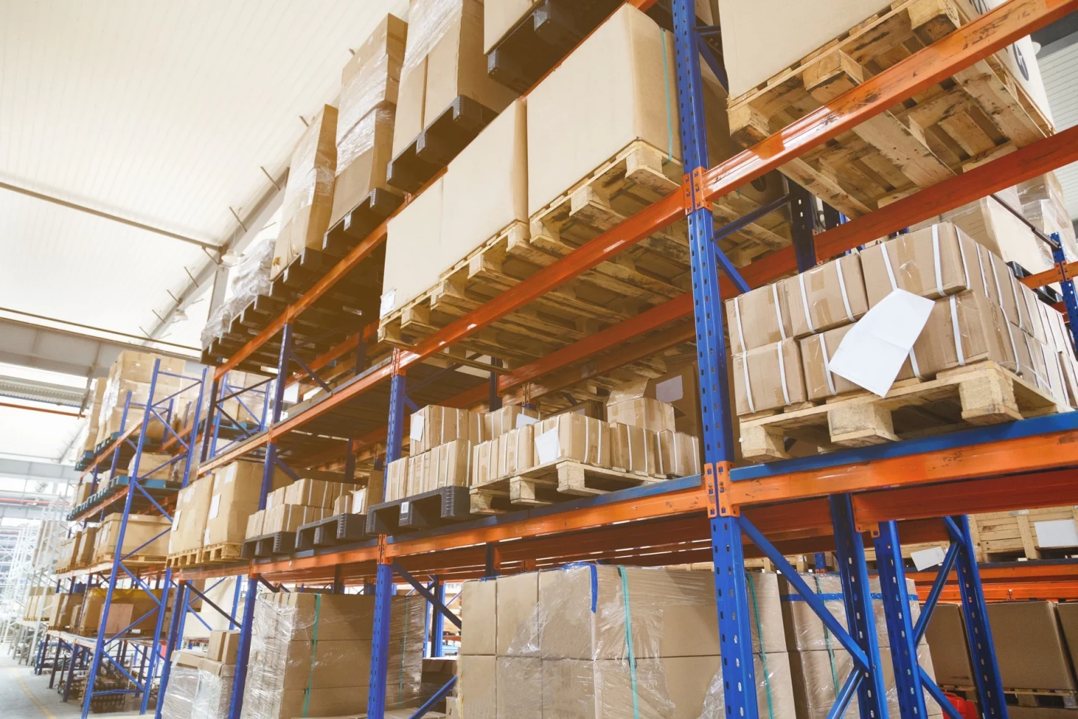 Étagères d'entrepôt chargées de cartons et palettes, illustrant un système de stockage ordonné pour la gestion des marchandises.