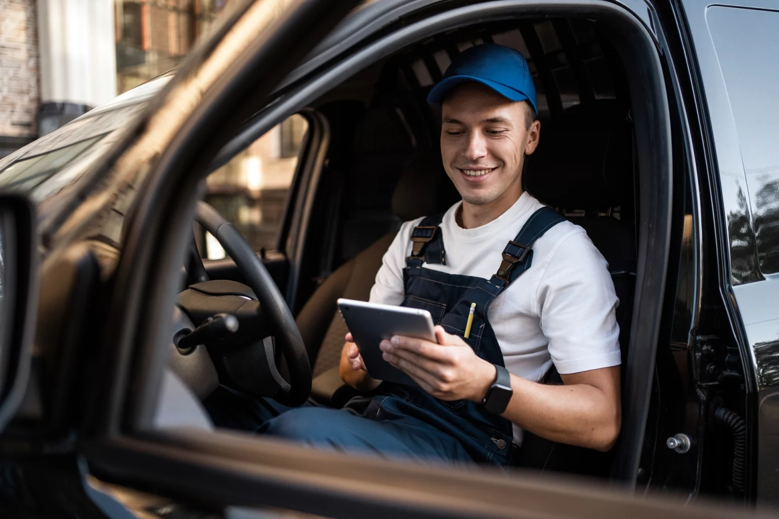 Un chauffeur-livreur souriant en uniforme, tenant une tablette électronique pour organiser ses livraisons, assis dans la cabine de son véhicule.