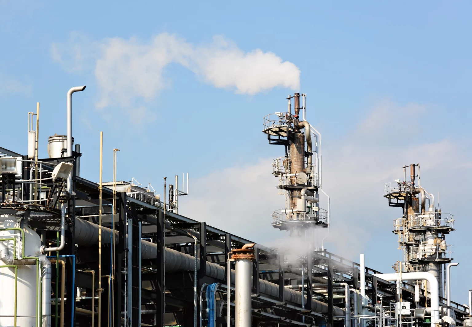 Installations industrielles du secteur de l'énergie avec des tuyauteries et des colonnes de distillation émettant de la vapeur, symbolisant l'industrie du gaz et de la pétrochimie.