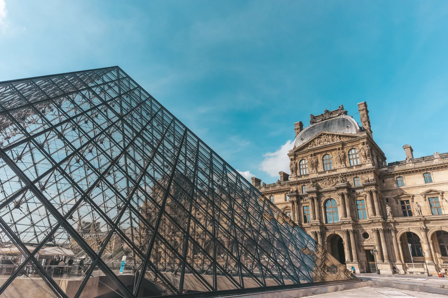 Musée du Louvre à Paris, structure en verre emblématique sous un ciel bleu, représentant le tourisme culturel et les monuments historiques.