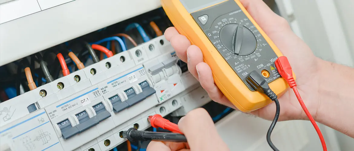 Technicien utilisant un multimètre pour tester ou diagnostiquer un panneau de commande électrique.