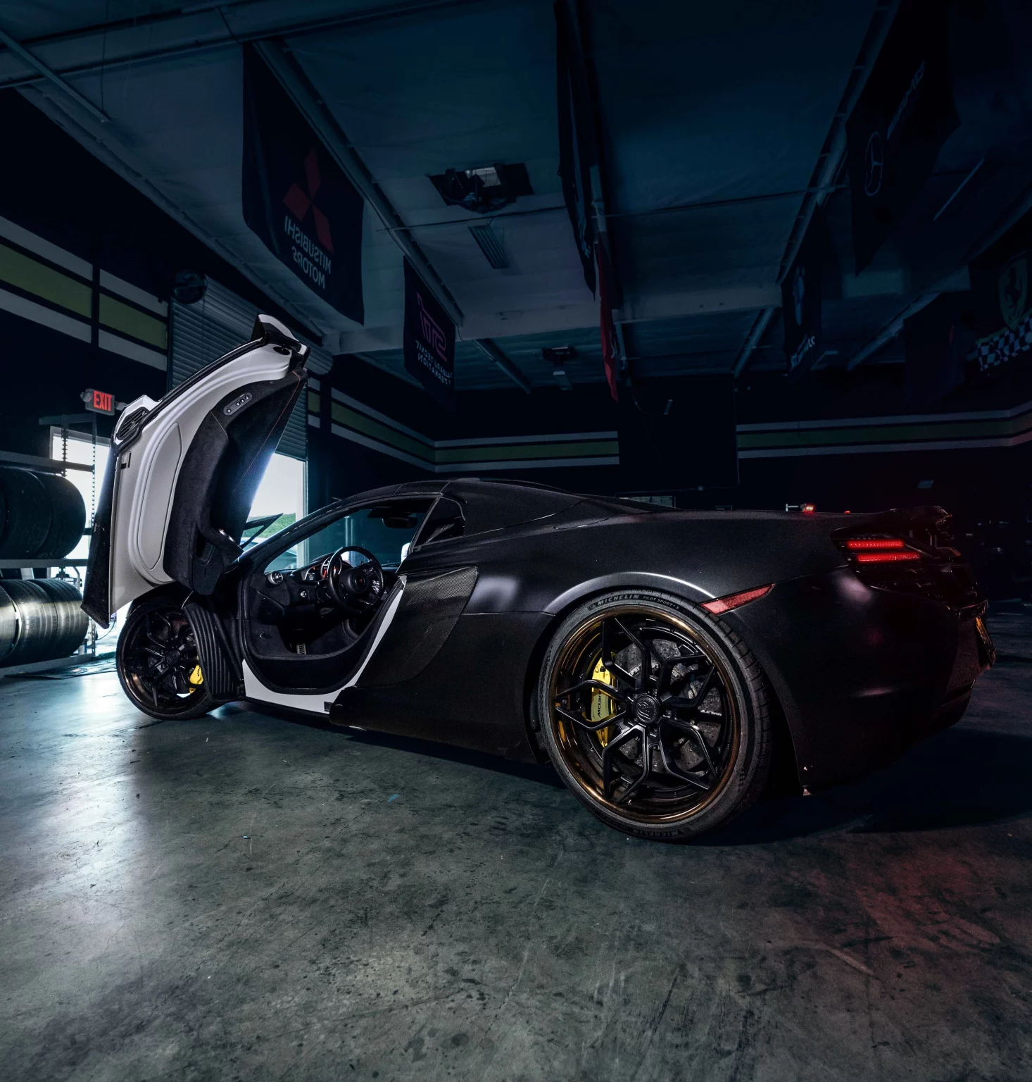 Voiture de sport de luxe noire avec portes papillon ouvertes dans un garage sombre.