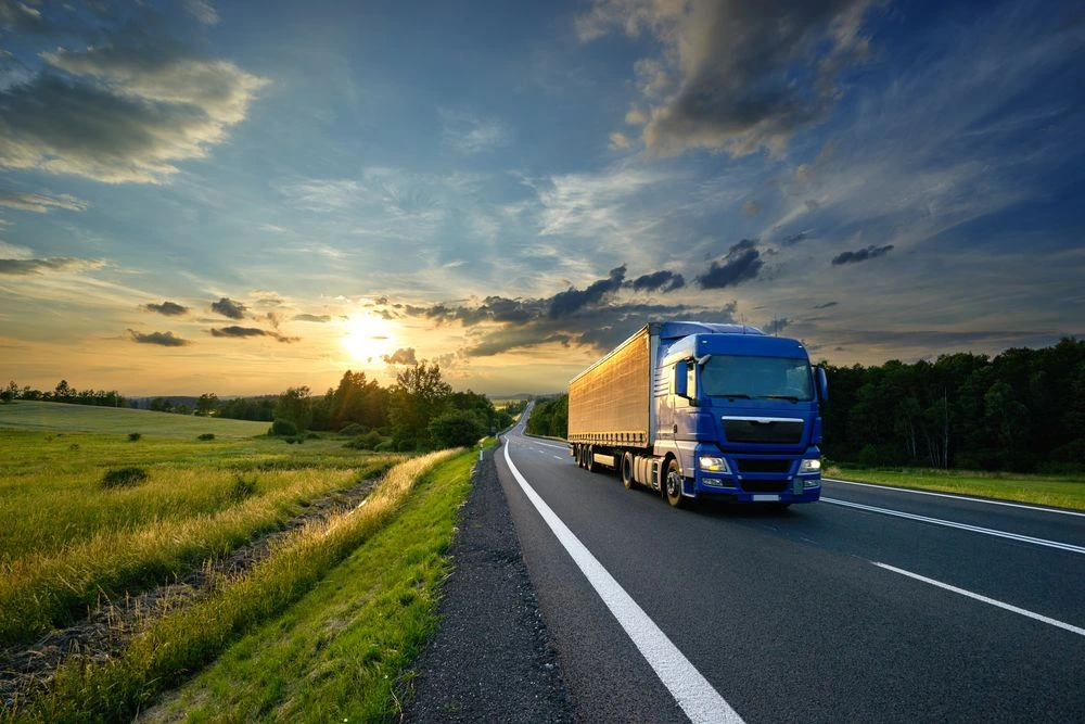 Camion bleu sur une route au coucher du soleil, représentant les services de transport routier de marchandises et la livraison longue distance.