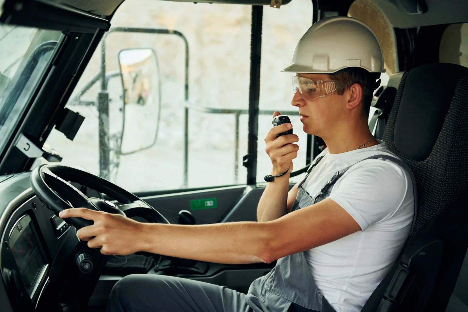 Chauffeur professionnel en uniforme conduisant un véhicule de transport lourd et communiquant via talkie-walkie, soulignant l'importance de la coordination dans la logistique.