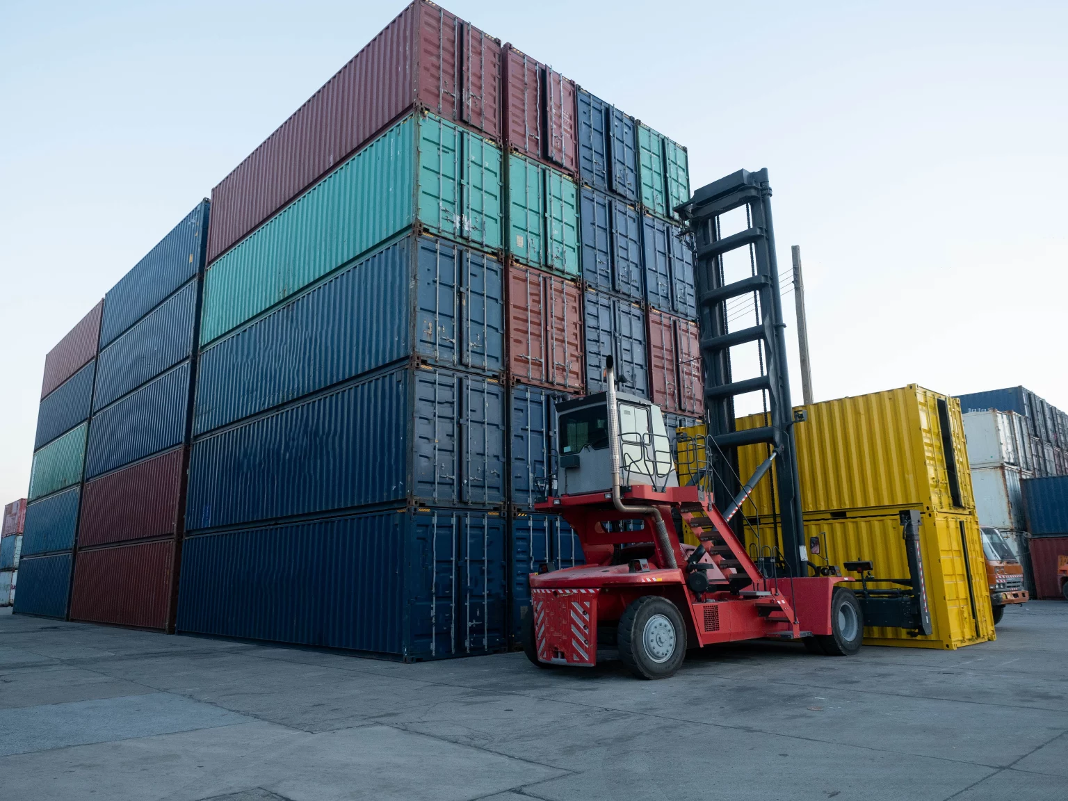 Chariot élévateur rouge manœuvrant des conteneurs de cargaison dans un terminal logistique, représentant les solutions de manutention et de stockage d'Innovia.