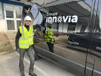 Chauffeur-livreur d'Innovia Transport en tenue de sécurité à côté d'une camionnette noire élégante portant la marque et les coordonnées de l'entreprise.