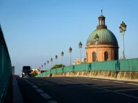 Un camion de livraison noir du "Groupe innovia" traverse un pont historique en pierre avec des lampadaires ornés et une balustrade verte. Le dôme d'un bâtiment historique est visible à l'arrière-plan, évoquant une ville européenne.